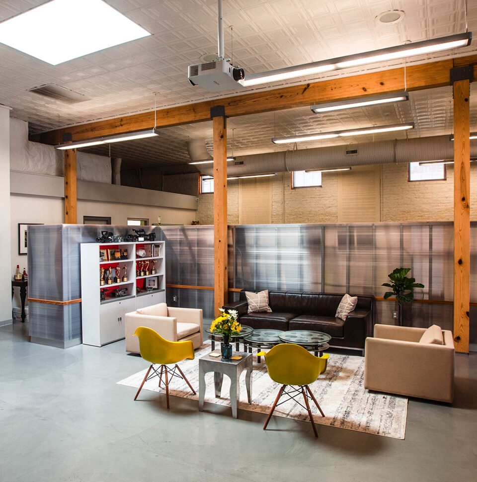 Lobby of Creative Bloc. One brown couch with two white chairs on either side. Two yellow chairs sit opposite the couch.